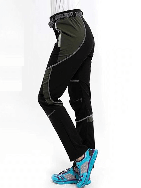 Side view of black and green women's hiking pants with quick-drying technology, worn with blue hiking boots.